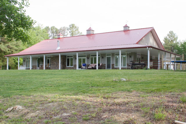 The rear view of the metal building home, featuring a spacious porch and a striking red roof.