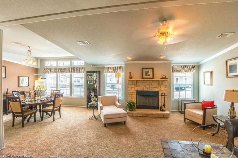 A spacious great room with a living area, kitchen, and dining area. The room is illuminated by chandeliers and has large windows that provide plenty of natural light and ventilation.