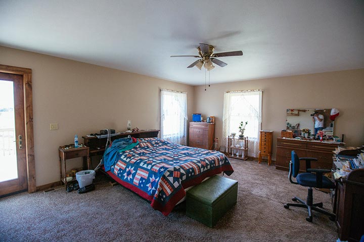 This spacious bedroom features a blue bed, plenty of natural light from the windows, and a desk for working or studying.