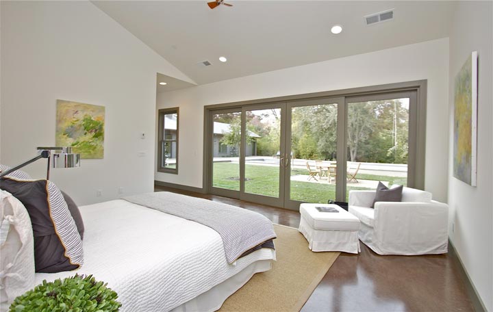 The master bedroom features a queen size bed, across it is a glass door leading to the backyard.