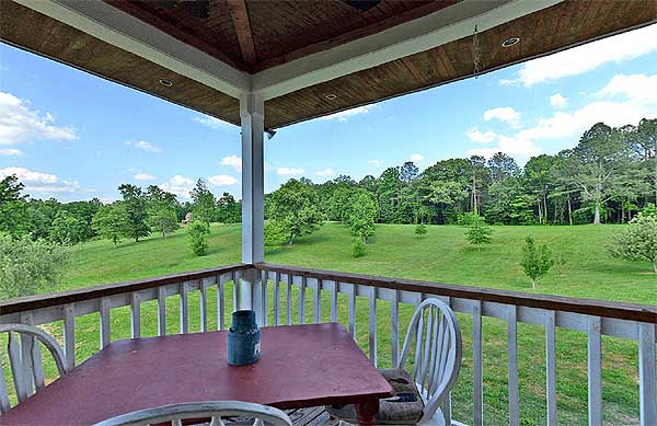 A table is set on the porch of a house, with a beautiful view of a field in the distance. 