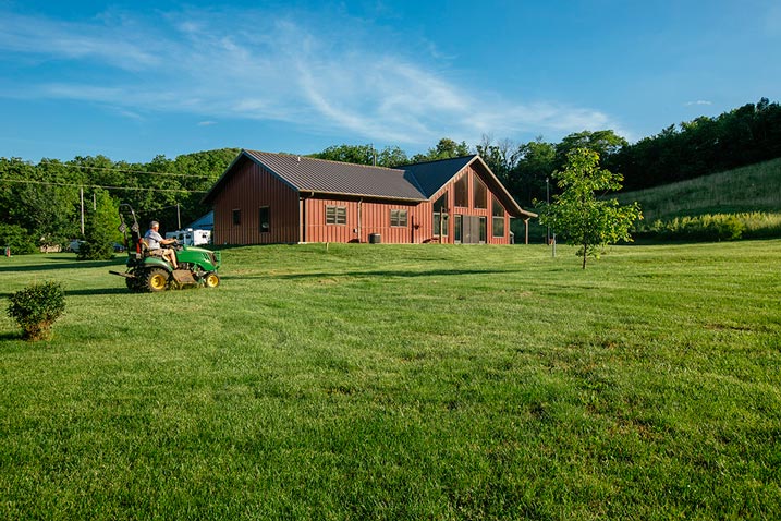 The metal building home sits on a wide green field. The building itself has a sleek, modern design that stand out against its surrounding landscape