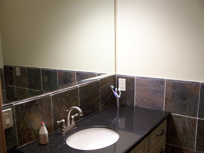 This image shows a bathroom sink with a marbled counter top. Above the sink is a large mirror, for grooming and getting ready in the morning.