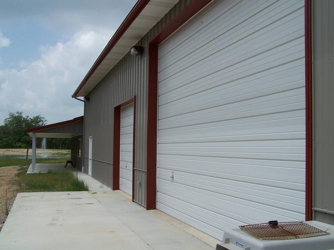White garage Doors with red trim on the right side of the barndominium.