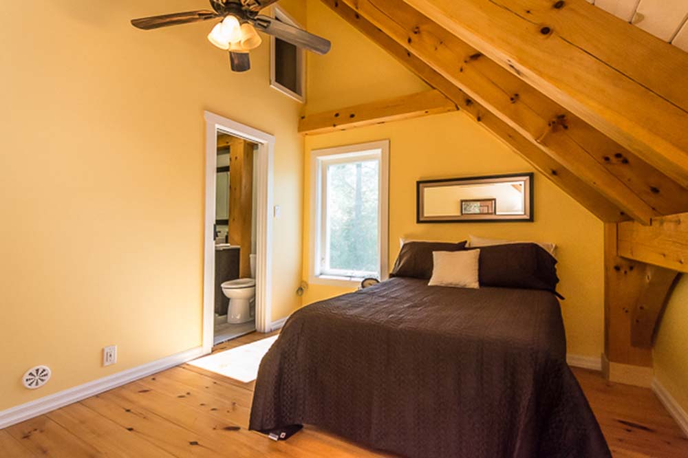 A cozy bedroom with wooden accents is situated next to a bathroom and features a window with natural light.