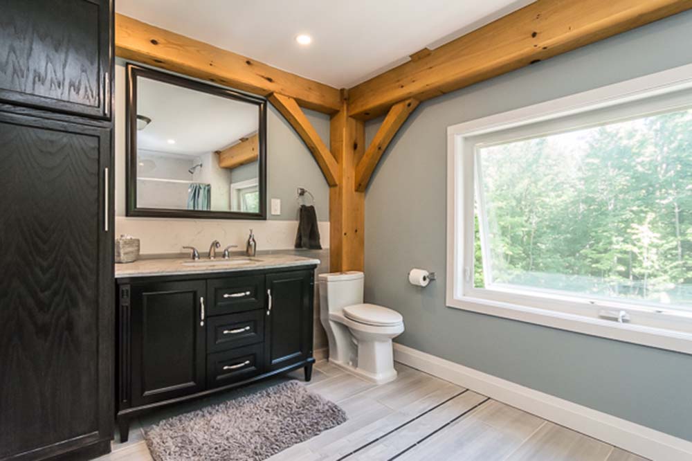 A gleaming bathroom features a toilet, sink with cabinet beneath a mirror, and a window providing natural light.