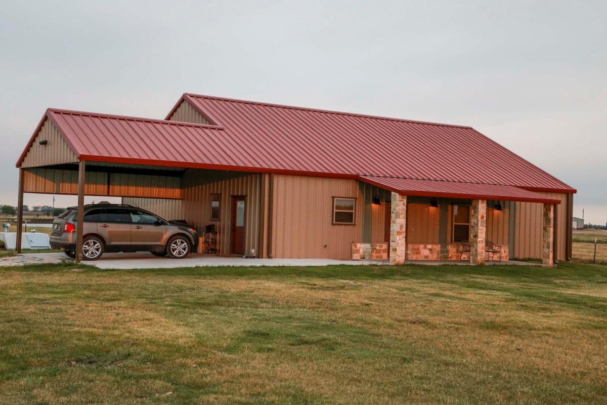 Side view of a metal building home with gabled red metal roof and a car port from Mueller Inc