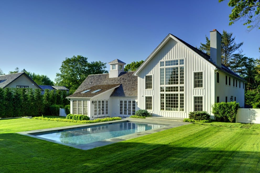 white elegant prefab barn home kit with a pool and a big green lawn by Yankee Barn Homes