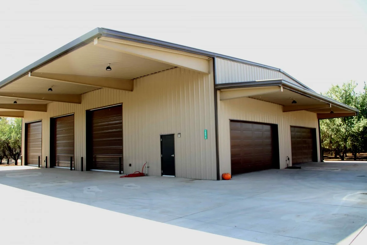 Metal building garage in light sand color exterior with six dark brown garage doors erected by Metallic Building Company