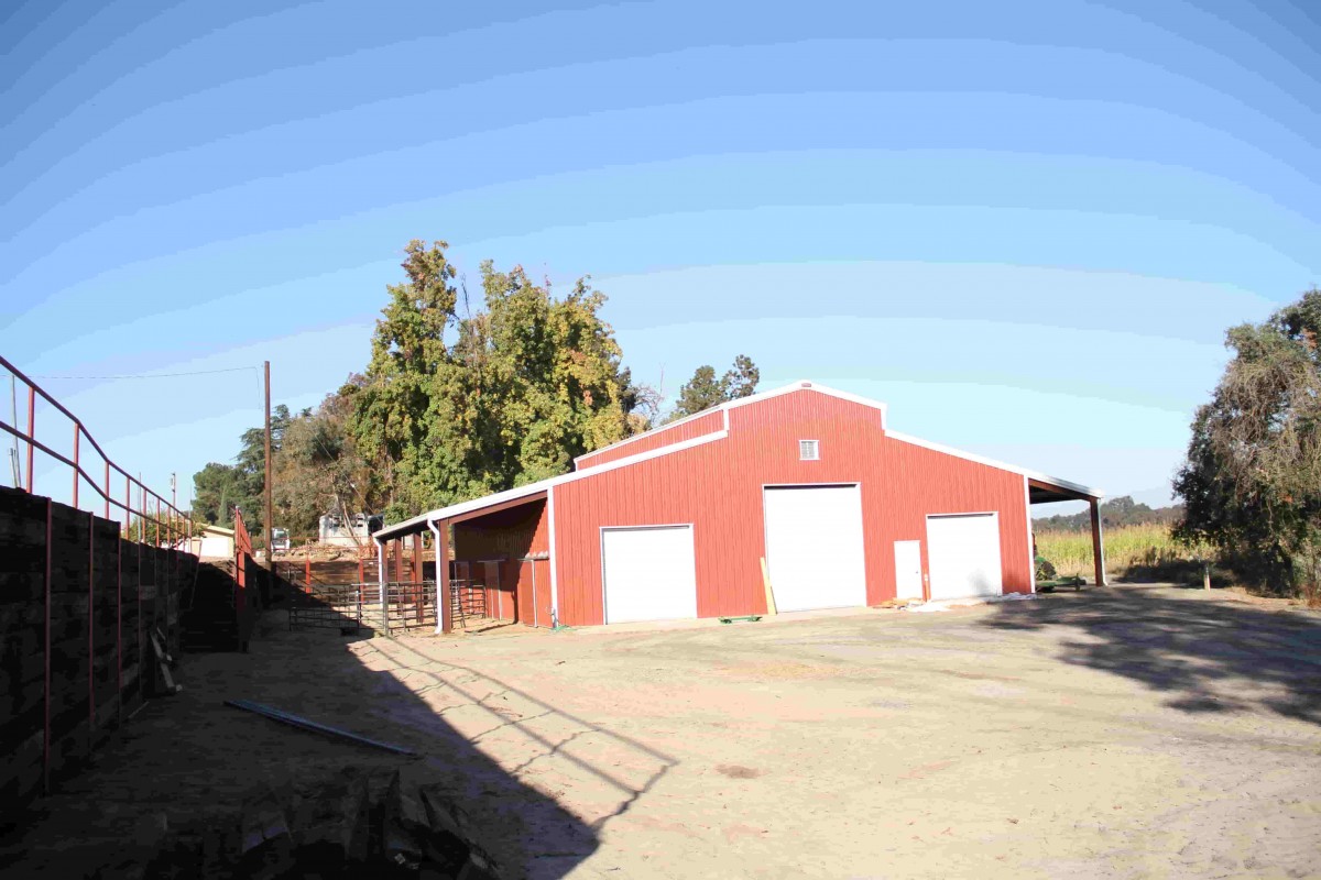Red metal barn building with three white doors and side porches built by Metallic Building Company