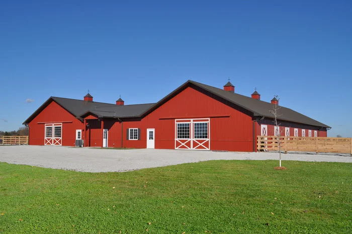 Post-frame horse stall with living quarters in bright red color and two sliding barn doors constructed by Wick Buildings