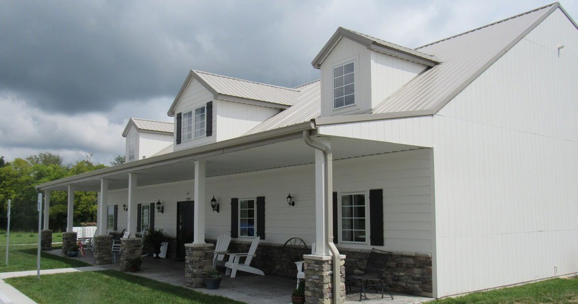 Angled front-right view of a two story metal building home showing the porch with white wooden columns from world wide steel buildings