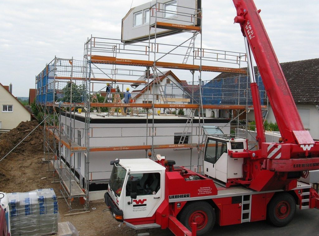 The building process of prefab home with big red crane and lots of scaffoldings 