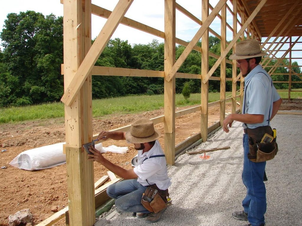 Two amish with hats  building a wooden side wall of the pole barn.