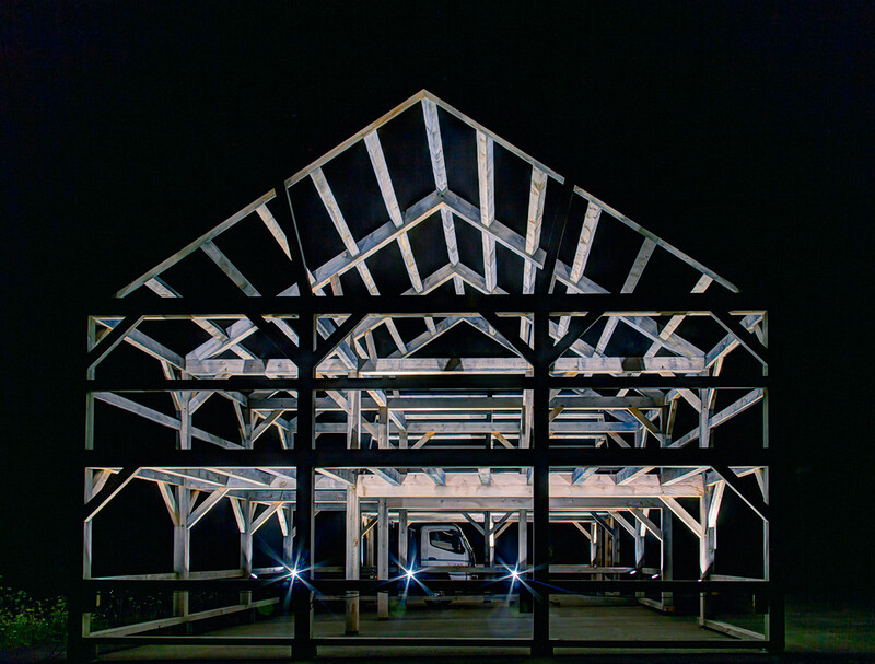 Beautiful pole barn wooden frame at night lit by flashlights in the pitch black background.