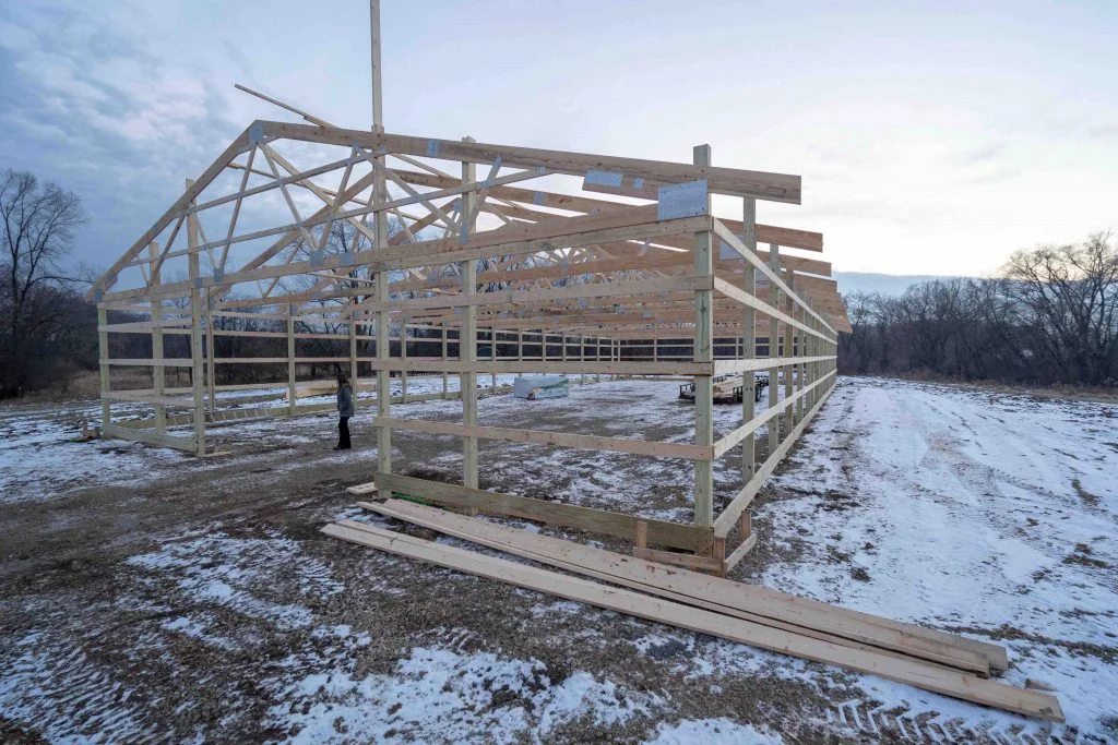 Early stages of wooden pole barn frame erection in winter time.