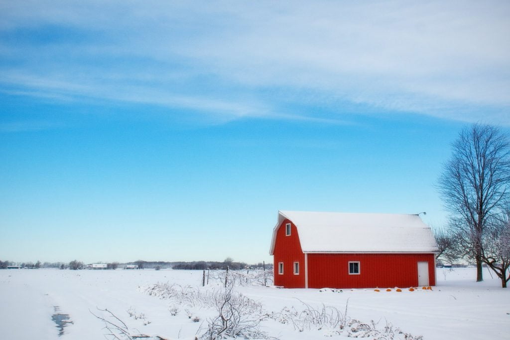 Red gambrel-type pole barn in snow covered field and blue sky.