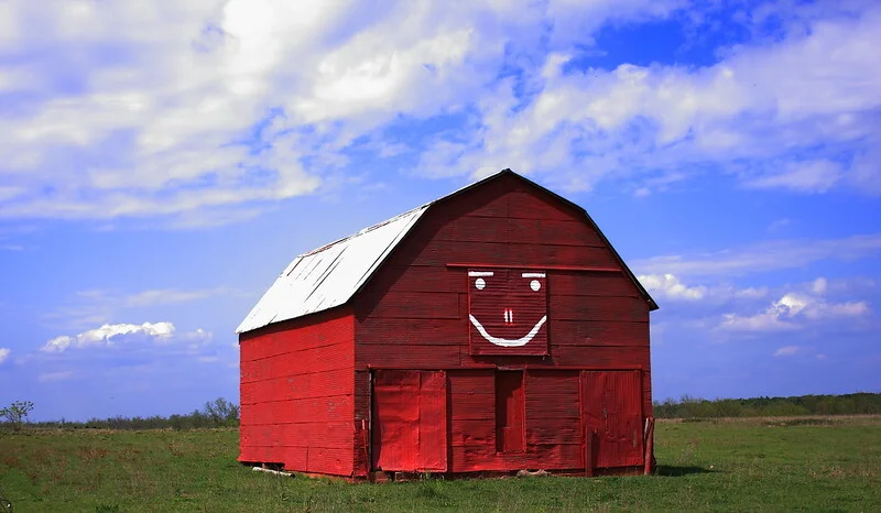 Red old gambrel-style pole barn in the middle of nowhere with a smiley face on it