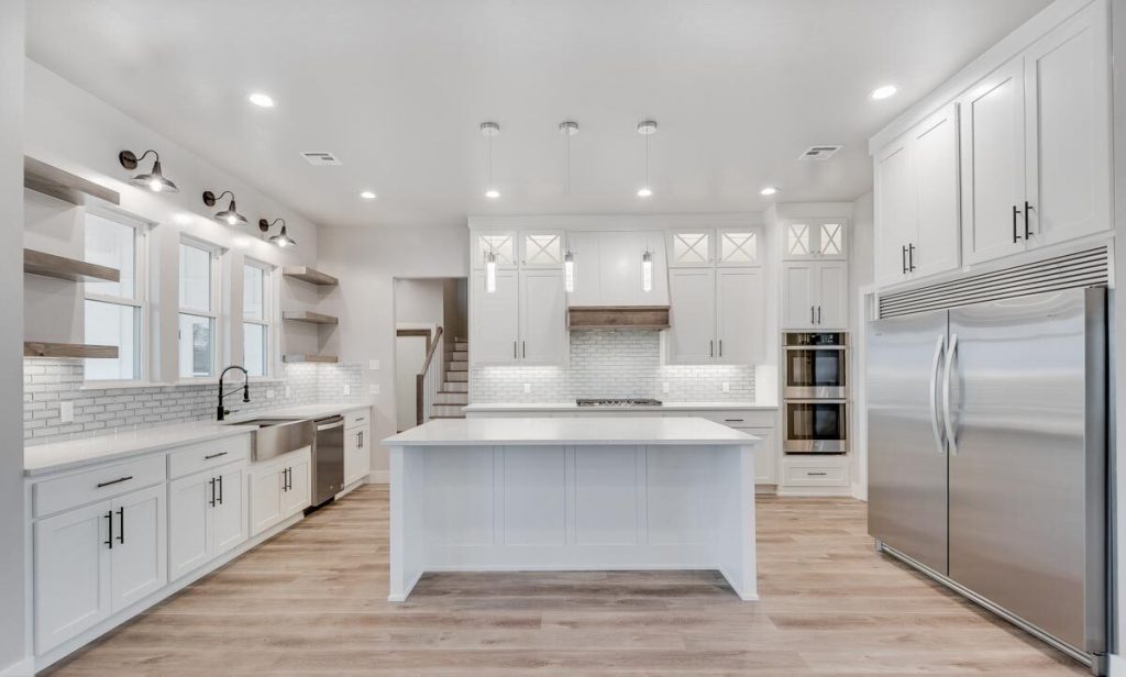 Well-lit wide kitchen with a large island in the middle, and white cabinets.