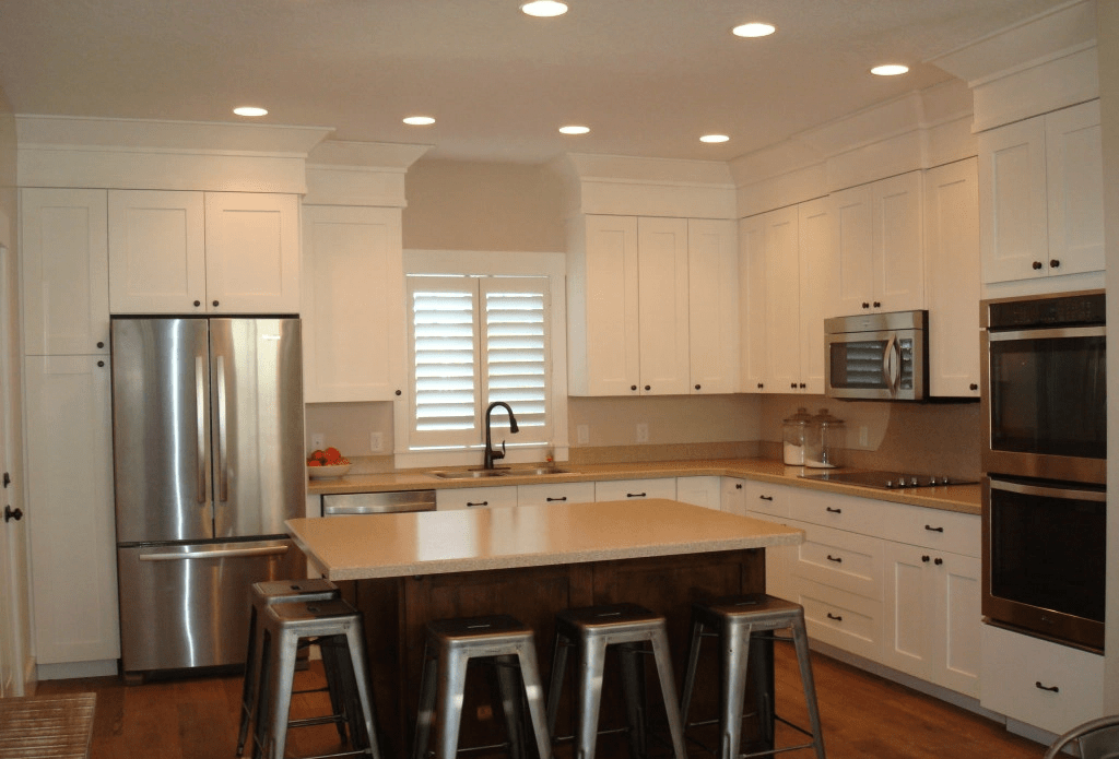 Kitchen equipped with a breakfast island in the center and eating area for 5 stools, two-door refrigerator, wall ovens, and dim yellow lights.