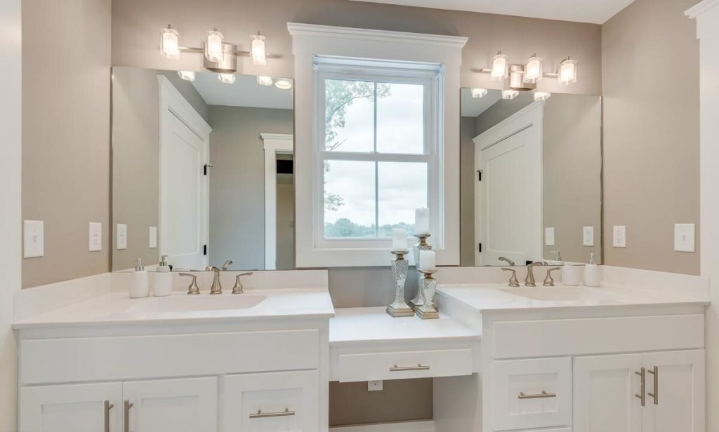View of the bathroom sink with mounted mirrors, white drawers and a window in the middle 