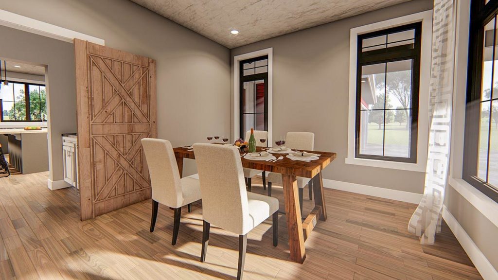 Angled view of the dining area w/ wooden flooring, barn-style door, recessed lights, and white trim. Also with wooden dining table at the middle of the room, it has 4 upholstered chairs.