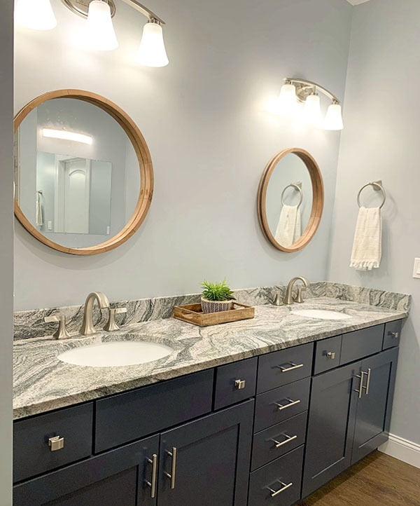 Marble countertop with two sinks, round mirrors, and wall mounted lights.
