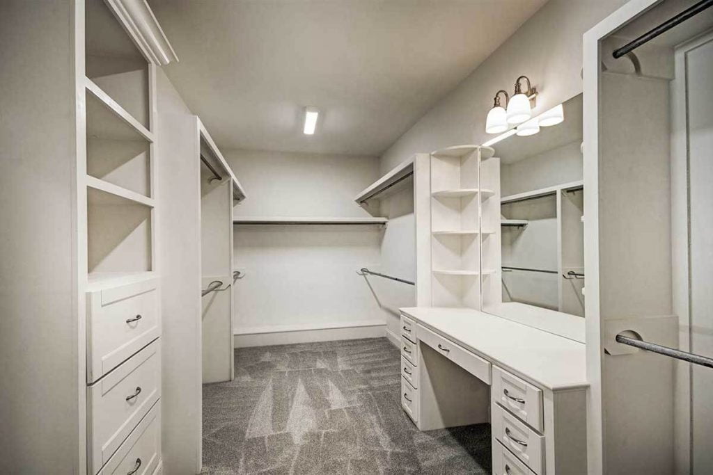 Master closet with clothe racks and drawers, desk and wall mirror.
