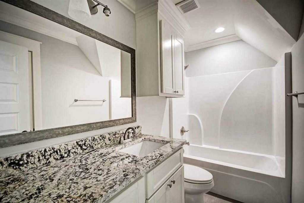 Bathroom with toilet, bathtub, and shower, marbled countertop with sink, and a wide wall mirror.
