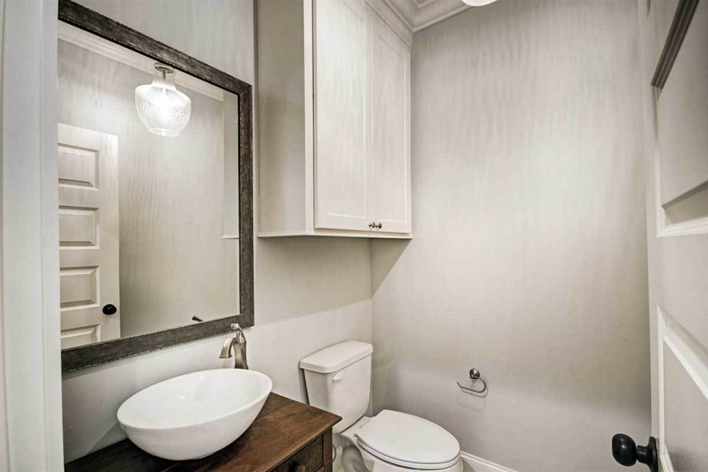Comfort room with toilet, sink, cabinets, and a wall mounted square mirror.