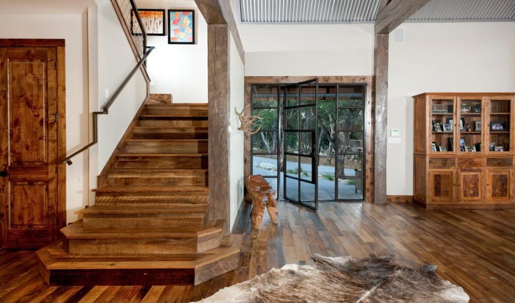 The hall shows wooden stairs to the 2nd floor, an animal rug, the front porch's glass door, and a wooden cabinet