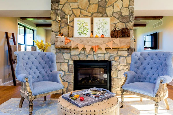 Great room with a stone fireplace, furnished with tufted armchairs and a round ottoman.