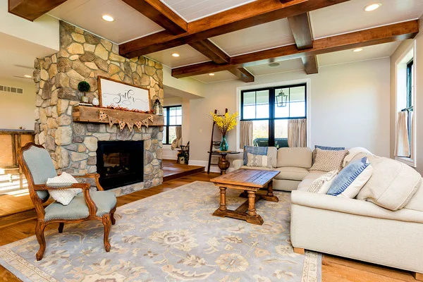 The family room has a beamed ceiling and is furnished with an upholstered chair, an L-shaped sofa, and a wooden coffee table over a floral area rug.