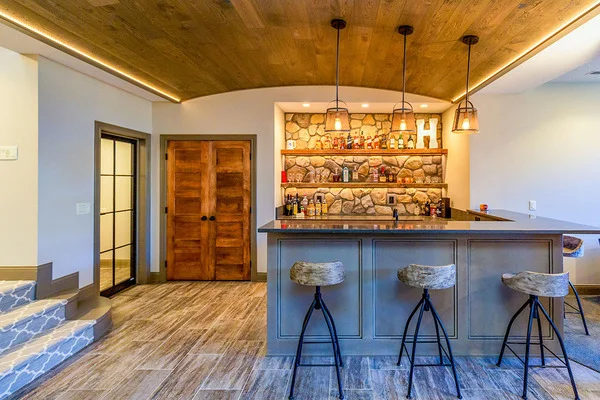 An L-shaped wet bar under a barrel-vaulted ceiling with round stools, and wooden shelves against the wall.