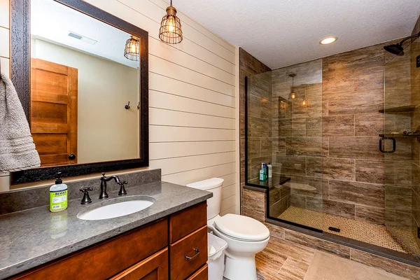 The bathroom with a walk-in shower, a toilet, a sink, and a framed mirror.