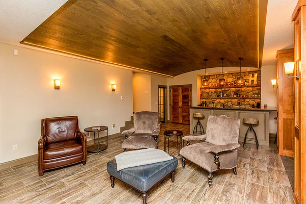 Room with a barrel-vaulted ceiling, wet bar, armchairs, and an ottoman.