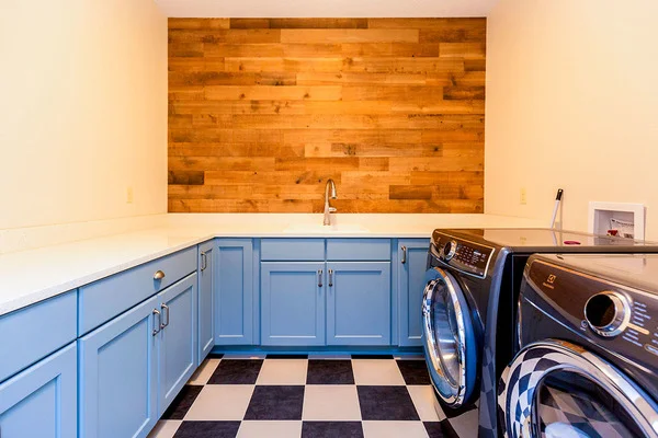 Utility room equipped with front load appliances, and marble countertops with blue cabinets.