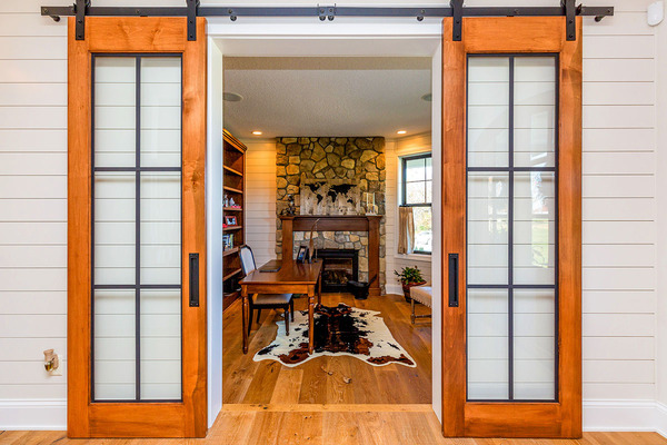The barn-style door opens to the den with its own stone fireplace and is furnished with wooden furnitures.