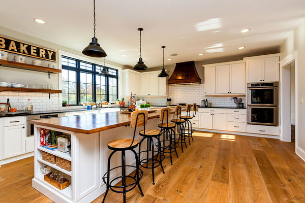 The kitchen is well-lit and is equipped with white cabinetry,  stainless steel appliances, subway tile backsplash and a long center island ith 6 stools.