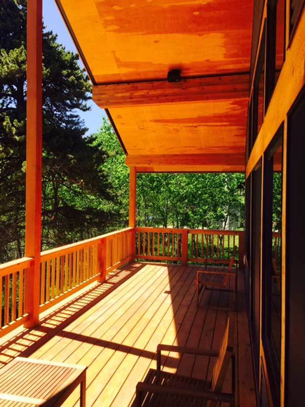 Covered deck enclosed in wood railings and roof supported by wooden columns.