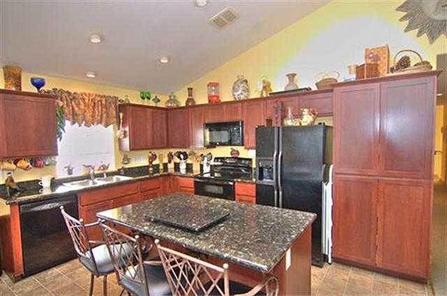 The kitchen is equipped with an island bar for 3 stools, wooden cabinetry, and metal appliances.