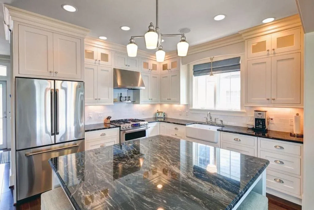 The kitchen equipped with a granite top island, white cabinetry, and stainless-steel appliances.