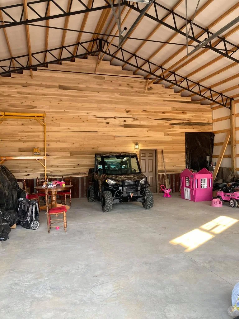 A wide garage with ample space for storage and organization. The floor is cluttered with various toys, including cars and action figures. A sleek black car is parked in the center, shining under the bright overhead lights.