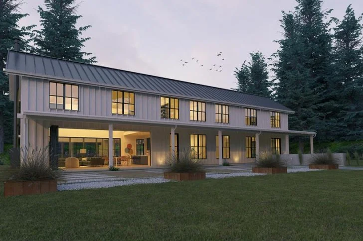 Side view of a large grey barndominium with large windows, spacious porch and lovely wooden pillars.