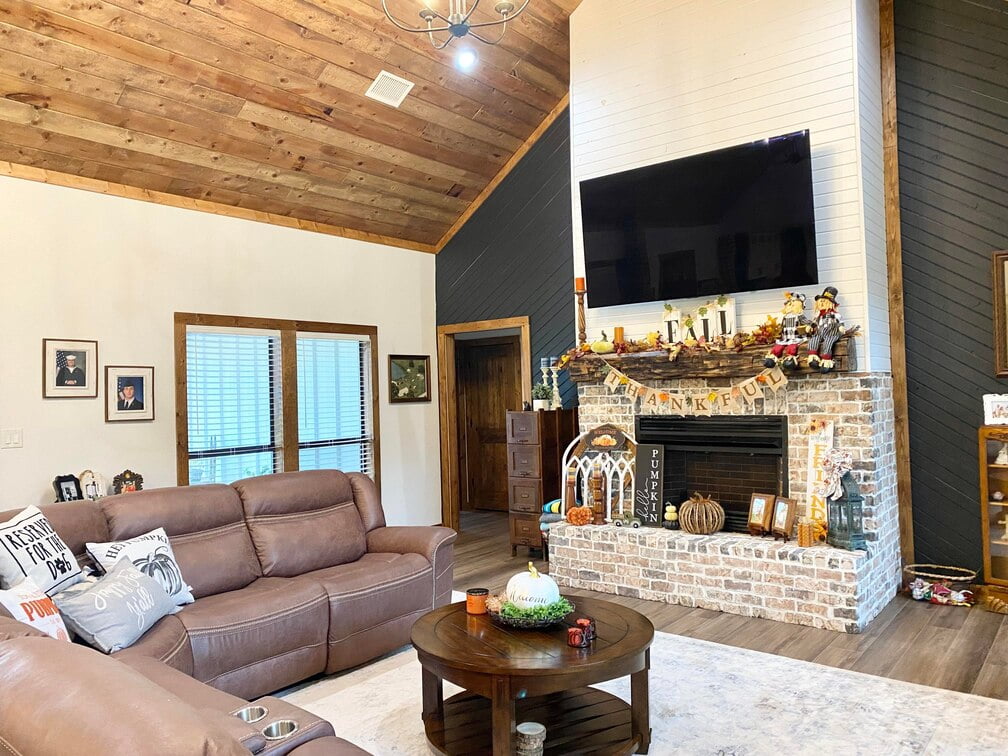 The Living area is furnished with leather sofa and coffee table that is sitting on a rug, stone fireplace, and a wall mounted TV. 
