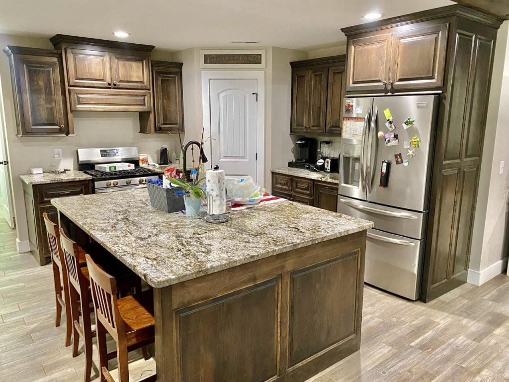 The kitchen is equipped with a square island, rustic cabinetry, and kitchen appliances.