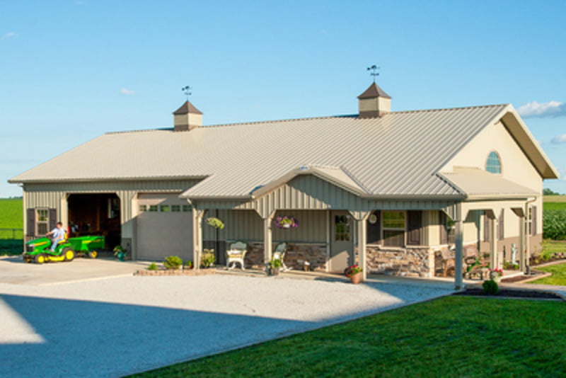 A peach barndominium building with a white garage door is shown. The roof is peach and a small truck is parked on the wide lawn in front of the building