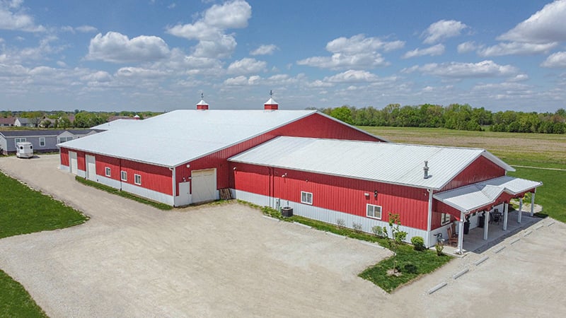 A white and red horse barn barndominium with a white roof and a large white garage door, set in a rural environment.