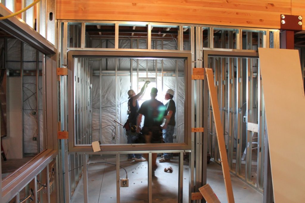 An image of the construction of a modular prefab home, with three people working together to design and build the structure. The prefabricated pieces of the house are clearly visible, and the team is hard at work putting it together.