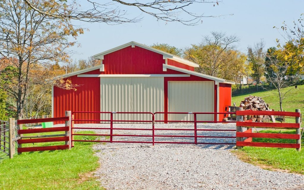 "A single story red and white barndominium with a white roof, set against a scenic rural background.
